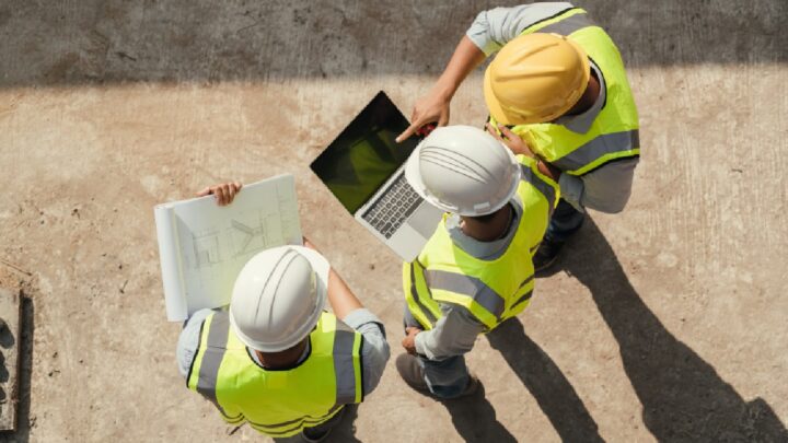 Construction site connectivity in action with workers reviewing plans and laptop on active job site