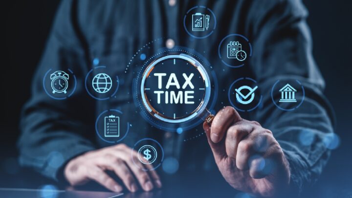 Person holding a magnifying glass over the words “Tax Time” with digital financial and compliance icons surrounding it, representing EOFY planning, tax preparation, risk management, and strong IT governance for business operations.